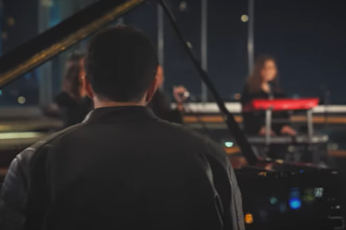 Pianist in dunkler Kleidung und im Hintergrund eine rot gekleidete S&auml;ngerin