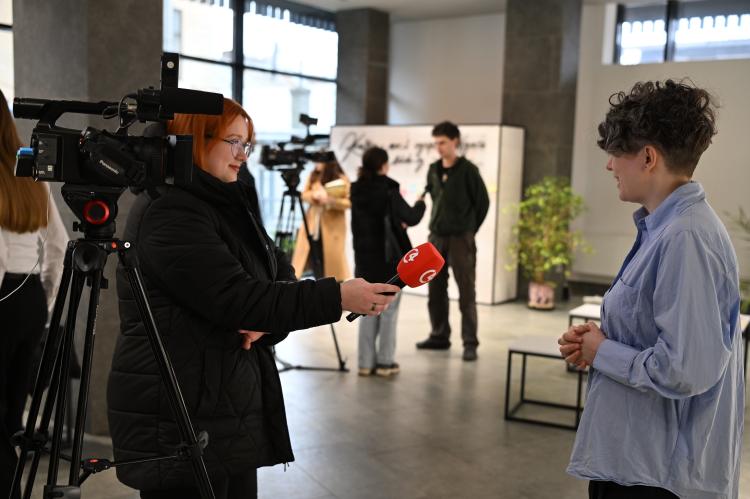 A journalist interviews Svitlana Osipchuk inside the exhibition space during the opening event