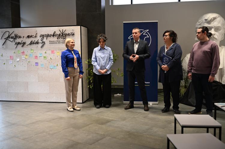 Speakers stand in front of an audience presenting the exhibition during the official opening