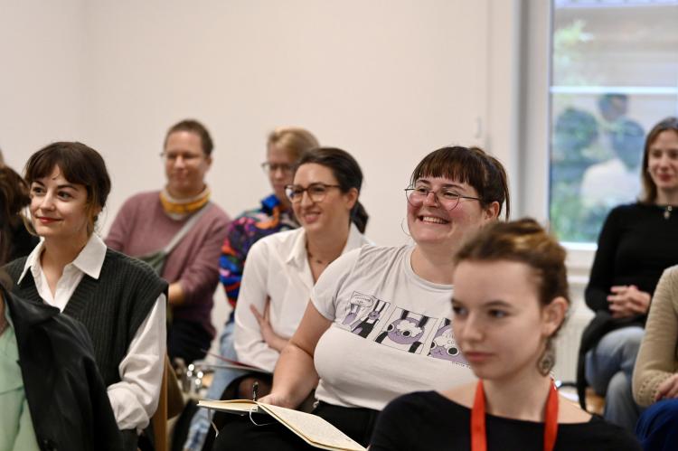 A group of young female artist listen to a stage discussion.