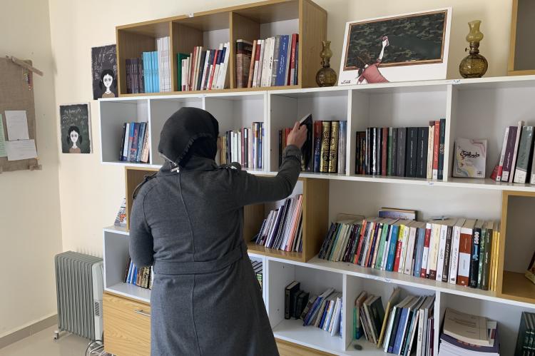 Woman standing in front of a bookshelf, reaching for a book