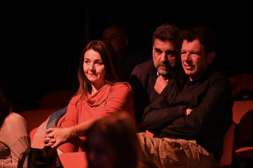 Drei Zuschauer*innen verfolgen eine Inszenierung mit kritischem Blick.