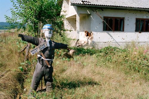 Eine Vogelscheuche, die als Peace Keeper der Vereinten Nationen verkleidet ist, vor einem Haus mit Einschussl&ouml;chern in der Stadt Kostajnica an der Grenze zu Kroatien in Nordbosnien.