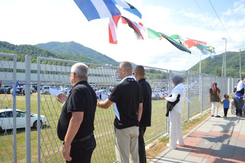 Besucher*innen der Gedenkst&auml;tte in Srebrenica lesen Postkarten, die an einem Zaun aufgereiht h&auml;ngen.