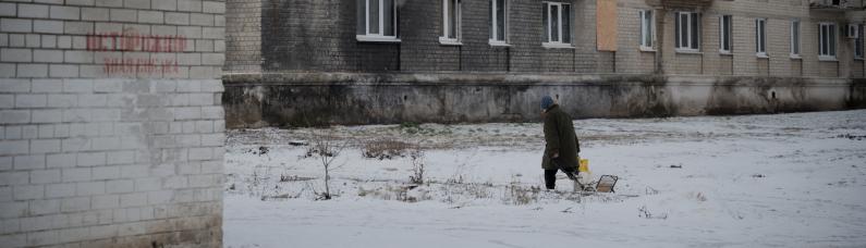 Eine Person l&auml;uft vor einem Haus in der Ukraine im Schnee.