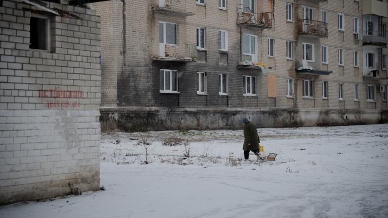 Eine Person l&auml;uft vor einem Haus in der Ukraine im Schnee.