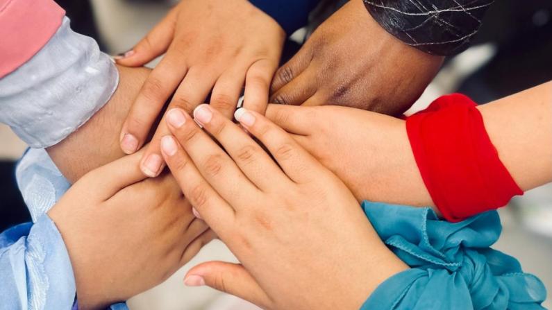 People stand in a circle and stretch their hands toward the center. They wear scarves around their wrists. People stand in a circle and stretch their hands toward the center. They wear scarves around their wrists.