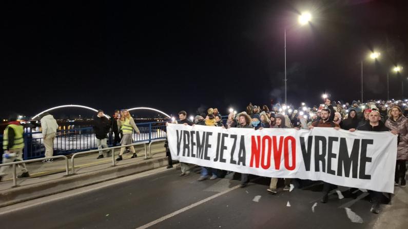 Ein Demonstrationszug zieht einen Banner tragend über eine Brücke.