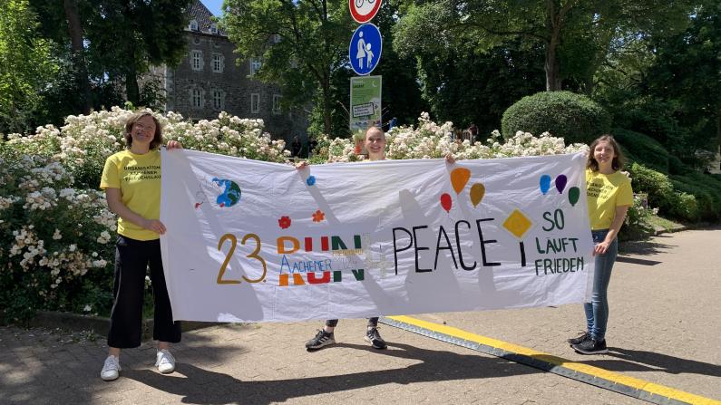 Startbanner des 23. Aachener Friedenslaufes Helfer*innen halten das Startbanner des 23. Aachener Friedenslaufes