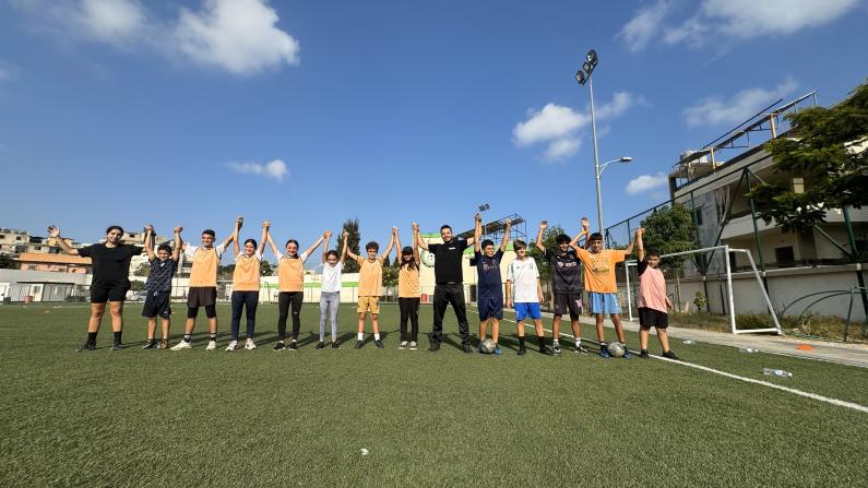 Coach with kids in field raising hands up