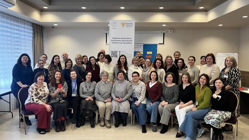 Group photo of over 40 participants of the Self-Support Leaders Conference in Kyiv, including self-support group leaders, psychologists, and community workers, standing and sitting together indoors in front of project banners.