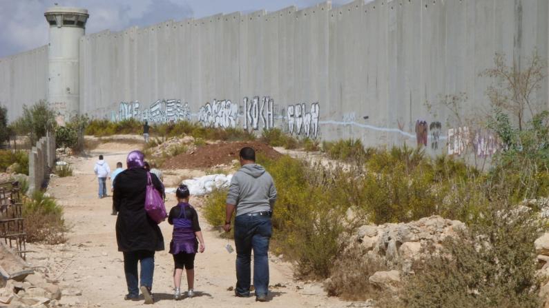 Eine Gruppe von Menschen läuft entlang ener Grenzmauer in Israel Eine Gruppe von Menschen läuft entlang ener Grenzmauer in Israel