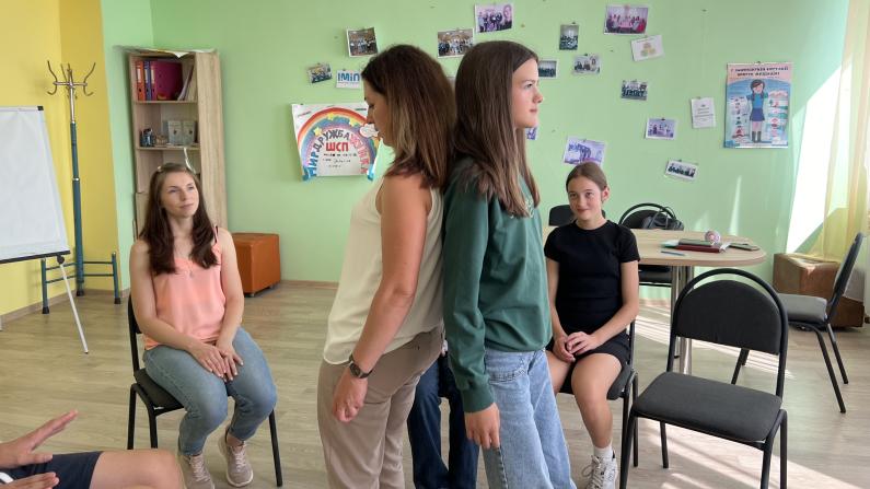 Zwei Schülerinnen stehen Rücken an Rücken und stützen sich gegenseitig während einer Einheit des "Peaceful School Project" Zwei Schülerinnen stehen Rücken an Rücken und stützen sich gegenseitig während einer Einheit des "Peaceful School Project"