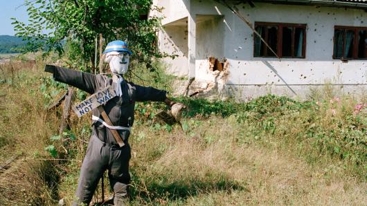 Eine Vogelscheuche, die als Peace Keeper der Vereinten Nationen verkleidet ist, vor einem Haus mit Einschussl&ouml;chern in der Stadt Kostajnica an der Grenze zu Kroatien in Nordbosnien.