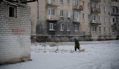 Eine Person l&auml;uft vor einem Haus in der Ukraine im Schnee.