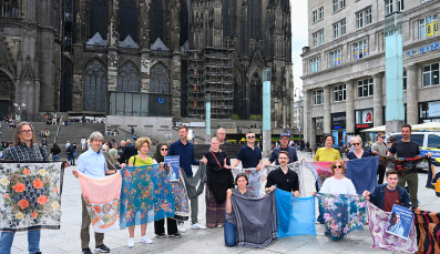 Anlässlich des 30. Jahrestages des Genozids von Srebrenica halten Mitarbeitende von Pro Peace Tücher und Schals vor dem Kölner Dom empor