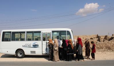 Frauen steigen in den Salam-Bus, der vor zuerstörten Häusern steht.