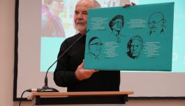 Gerold K&ouml;nig spricht vor Publikum und h&auml;lt ein Plakat mit Friedensaktivist*innen in die H&ouml;he.